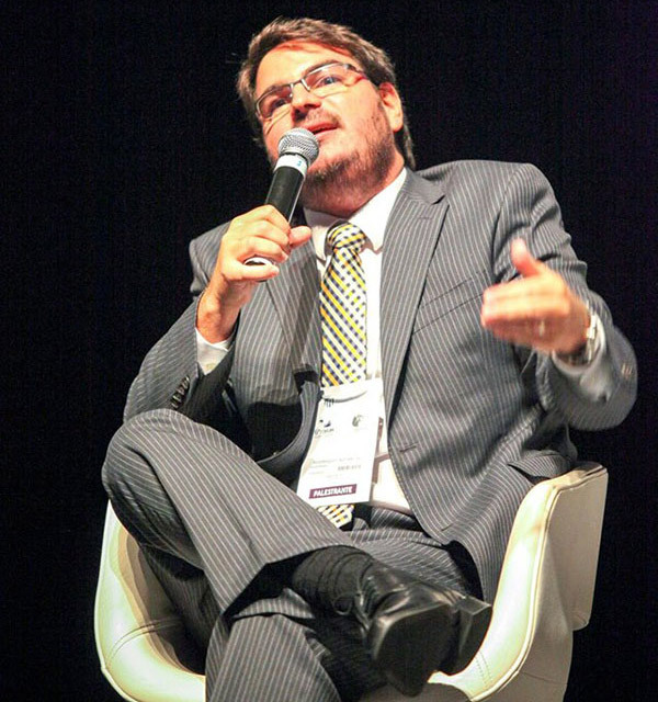 A photo of Rodrigo Constantino speaking at an event while seated and holding a microphone.